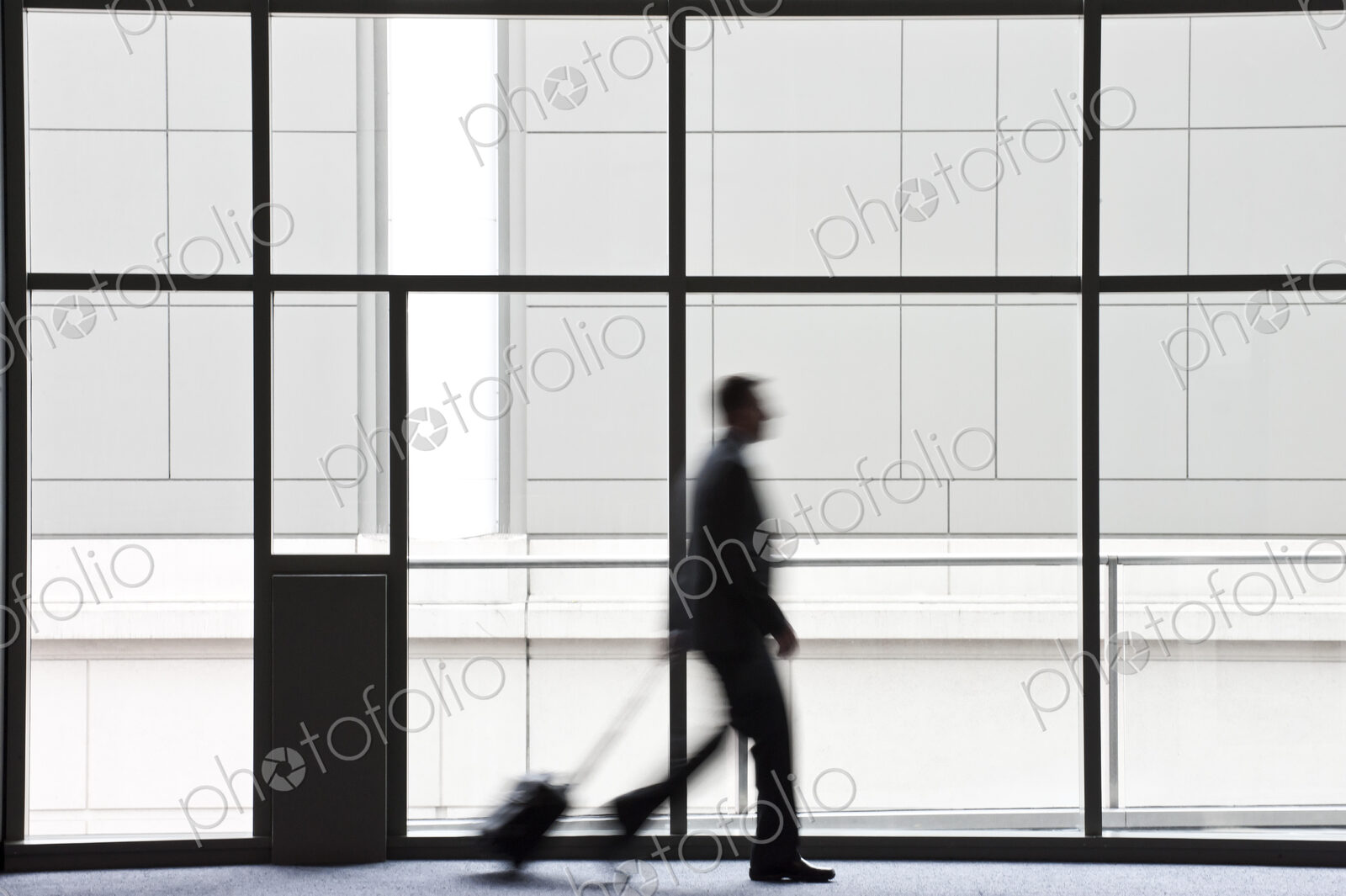 A businessman blurred in silhouette while walking past a large window in a convention…