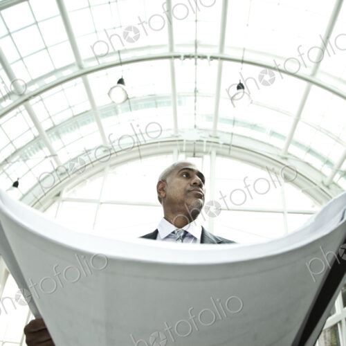 A businessman holding a large plan or architectural drawings standing under a glass… A businessman holding a large plan or architectural drawings standing under a glass…