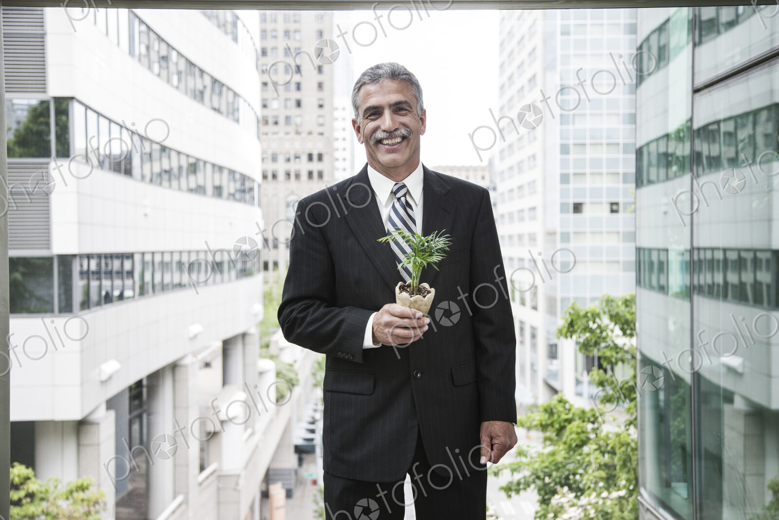 A businessman holding a small plant while stanidng next to a a large convention center…