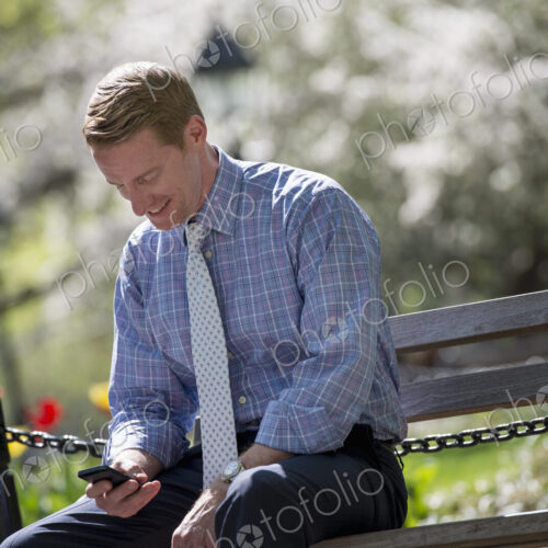 A businessman in a shirt with white tie, sitting on a park bench under the shade of a… A businessman in a shirt with white tie, sitting on a park bench under the shade of a…