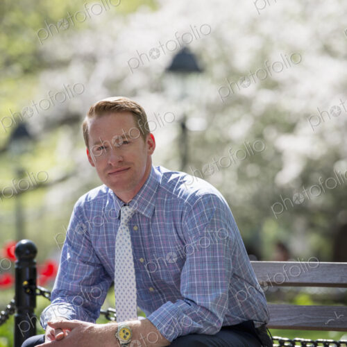 A businessman in a shirt with white tie, sitting on a park bench under the shade of a… A businessman in a shirt with white tie, sitting on a park bench under the shade of a…