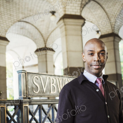 A businessman in a suit standing by a stairwell under an arched ceiling. A businessman in a suit standing by a stairwell under an arched ceiling.