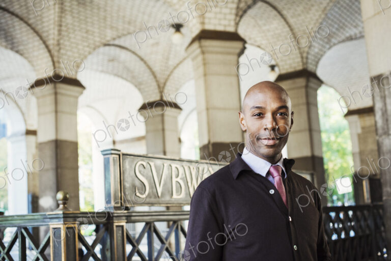 A businessman in a suit standing by a stairwell under an arched ceiling.