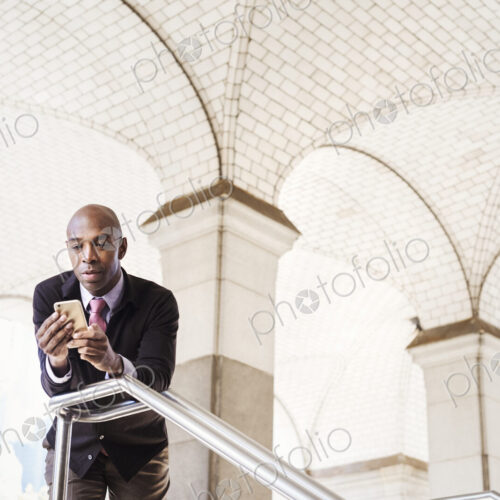 A businessman in a suit standing by a stairwell under an arched ceiling, checking his… A businessman in a suit standing by a stairwell under an arched ceiling, checking his…