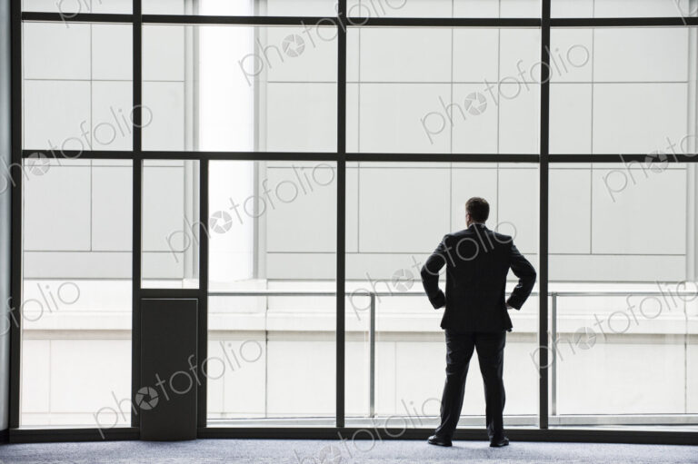 A businessman in silhouette standing at a large window in a convention center lobby.
