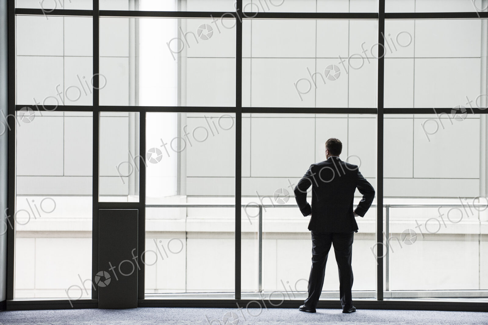 A businessman in silhouette standing at a large window in a convention center lobby.
