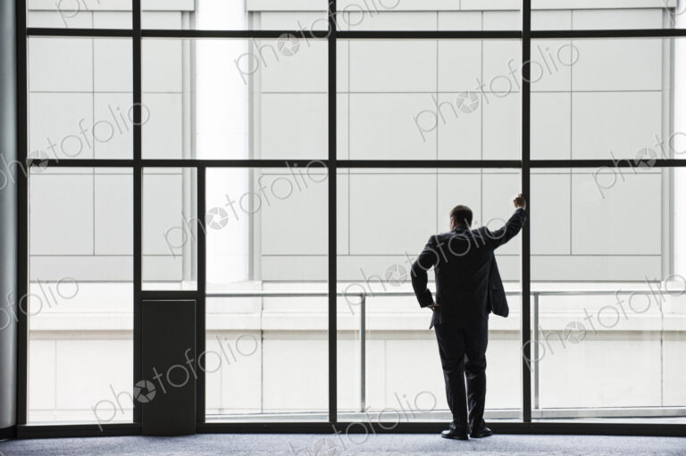 A businessman in silhouette standing at a large window in a convention center lobby.