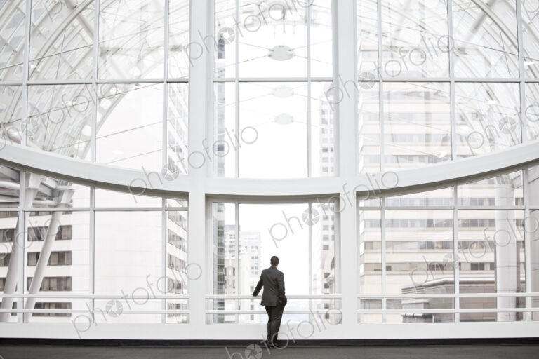 A businessman in silhouette standing at a large window in a convention center lobby.