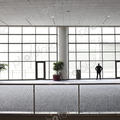 A businessman in silhouette standing at a large window in a convention center lobby.