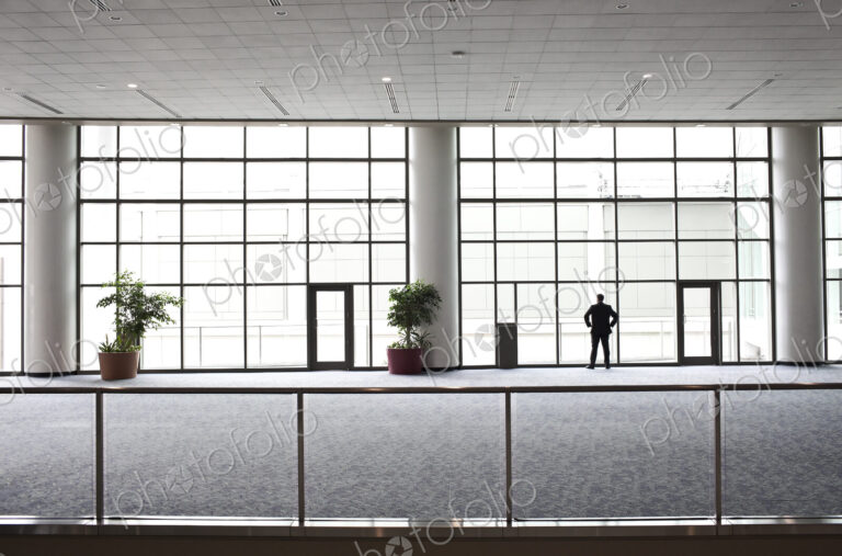 A businessman in silhouette standing at a large window in a convention center lobby.