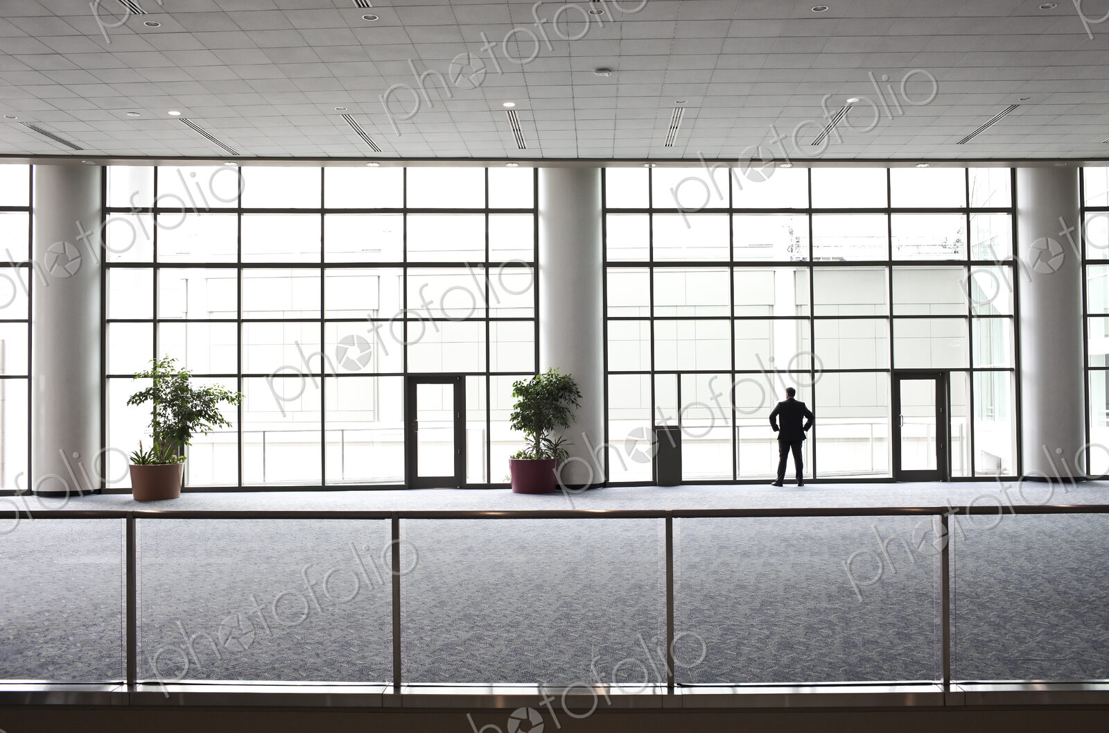A businessman in silhouette standing at a large window in a convention center lobby.