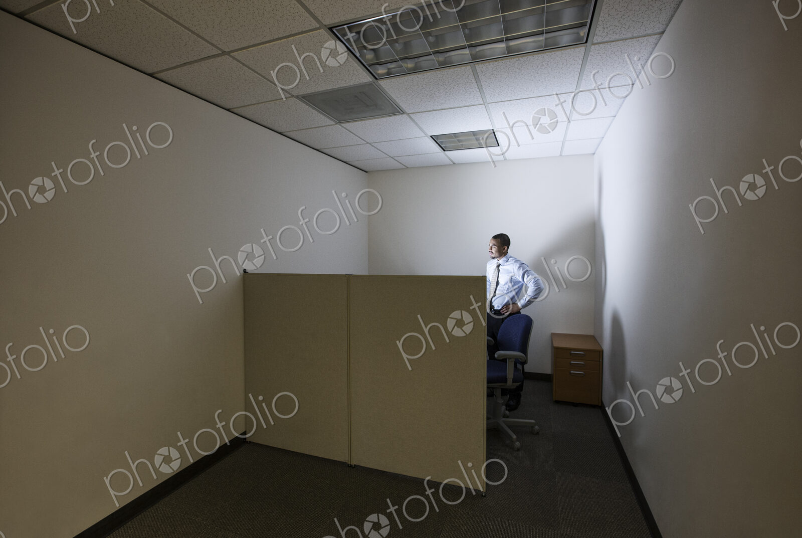 A businessman lit up by a computer screen in his small corner office cubicle.