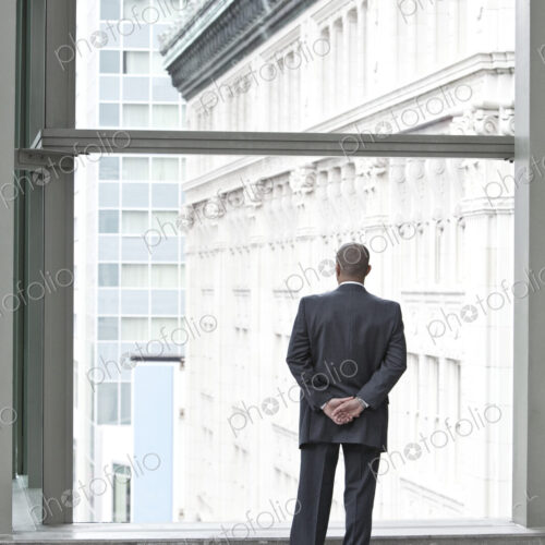 A businessman standing at a convention center window looking out the window at the… A businessman standing at a convention center window looking out the window at the…