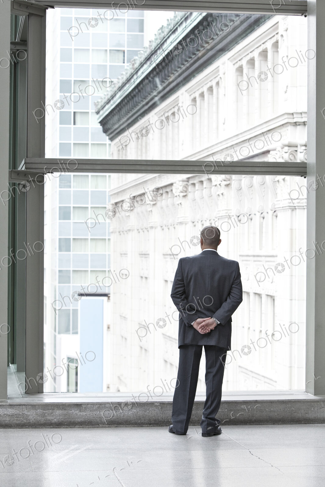 A businessman standing at a convention center window looking out the window at the…