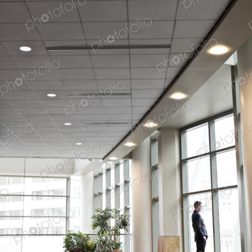 A businessman standing at a window in a large convention center lobby. A businessman standing at a window in a large convention center lobby.