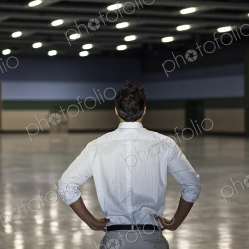 A businessman standing in a dimly lit and dark exhibition area in a convention center. A businessman standing in a dimly lit and dark exhibition area in a convention center.
