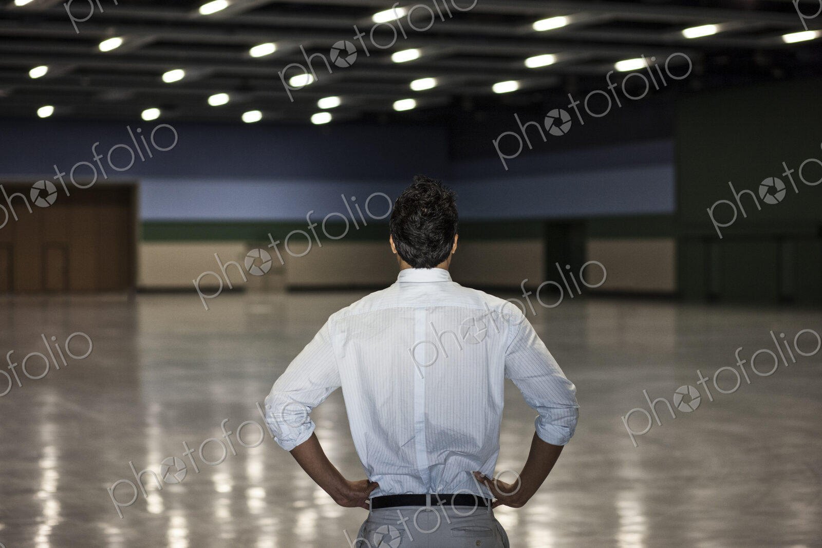 A businessman standing in a dimly lit and dark exhibition area in a convention center.