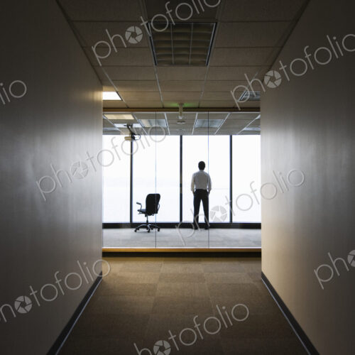 A businessman standing next to a window at the end of a long hallway. A businessman standing next to a window at the end of a long hallway.