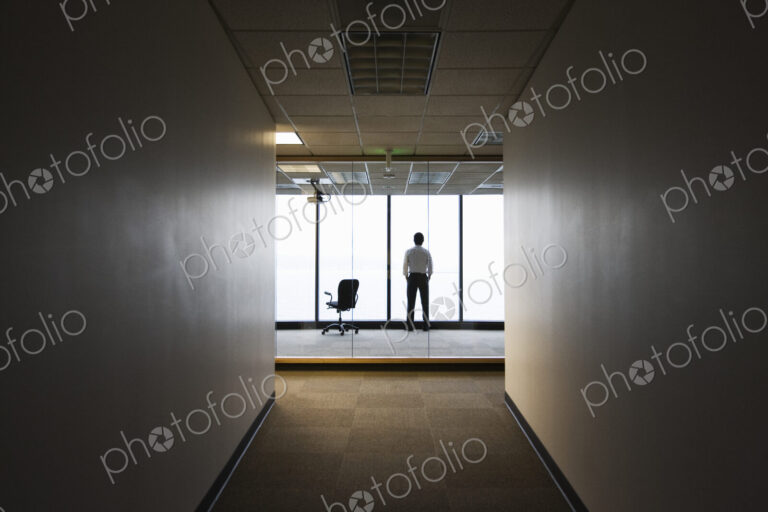 A businessman standing next to a window at the end of a long hallway.