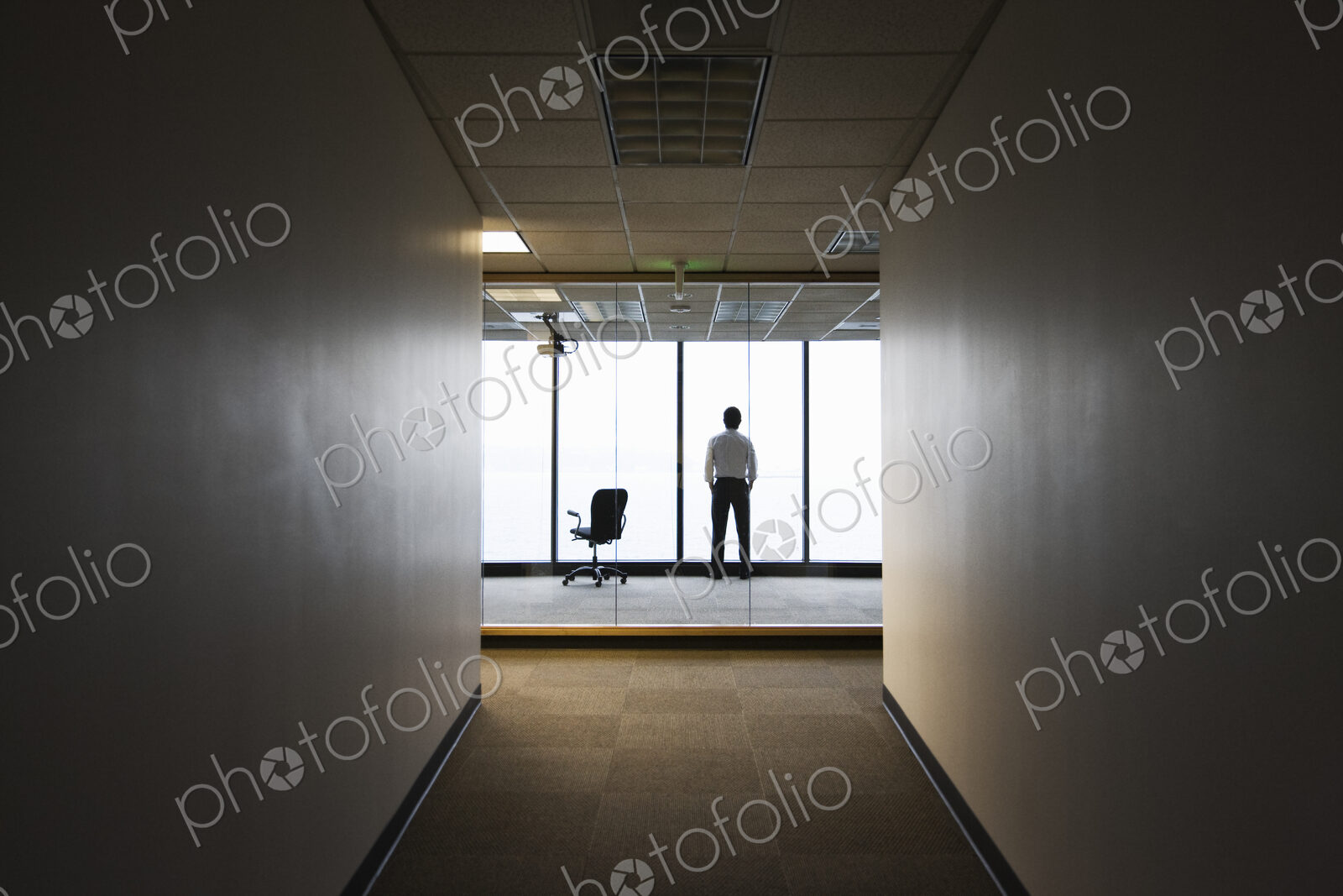 A businessman standing next to a window at the end of a long hallway.