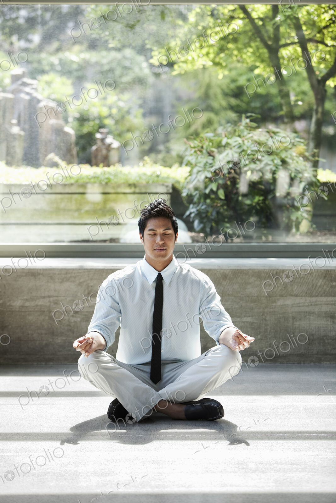 A businessman taking a meditative break in a room full of indoor plants.