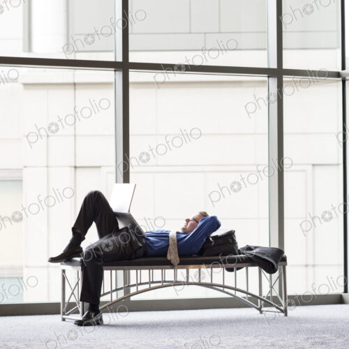 A businessman working on a laptop computer on a bench in a convention center lobby