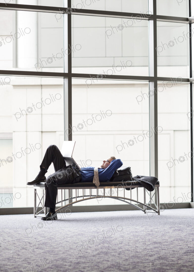 A businessman working on a laptop computer on a bench in a convention center lobby