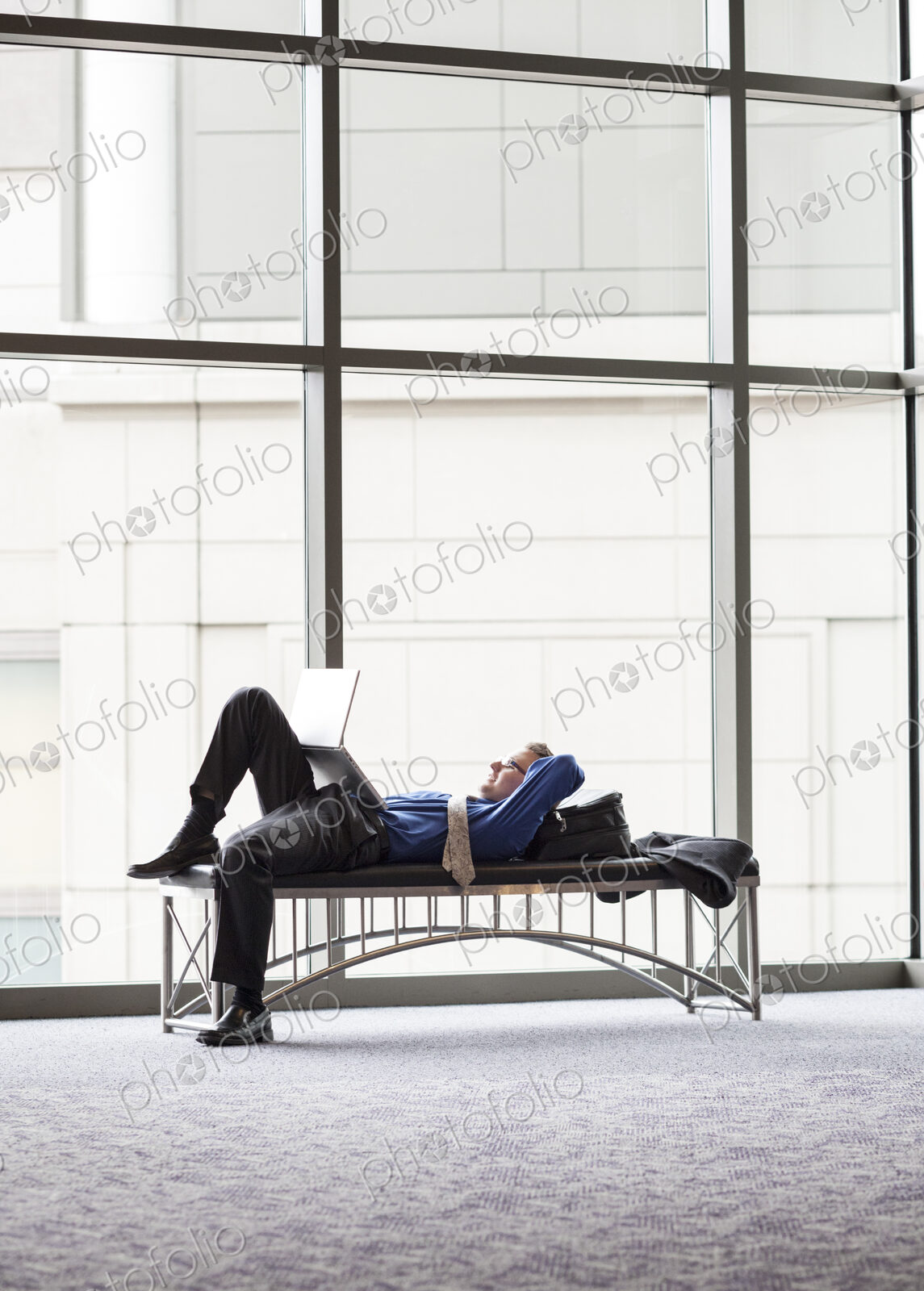 A businessman working on a laptop computer on a bench in a convention center lobby