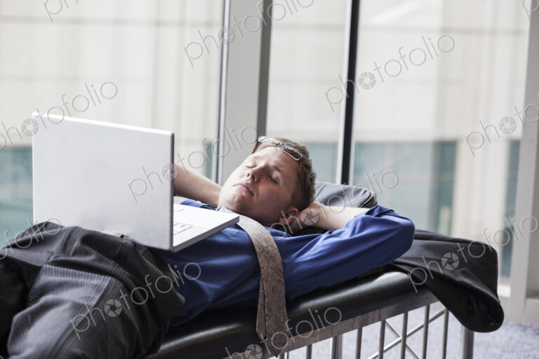 A businessman working on a laptop computer on a bench in a convention center lobby