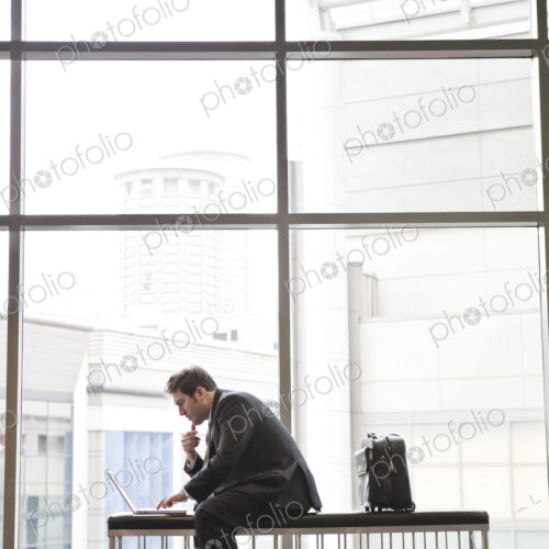 A businessman working on a laptop computer on a bench in a convention center lobby