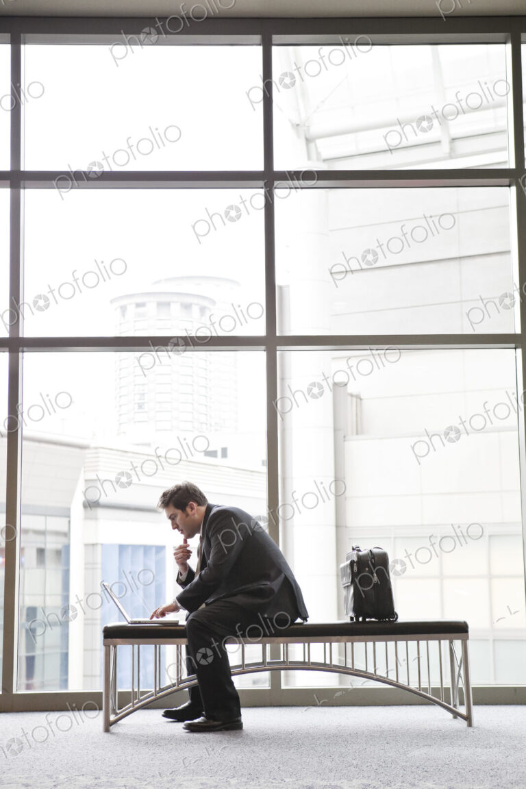 A businessman working on a laptop computer on a bench in a convention center lobby