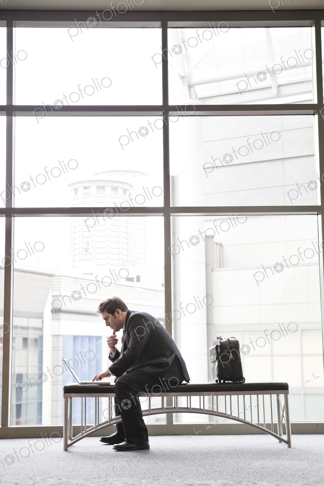 A businessman working on a laptop computer on a bench in a convention center lobby