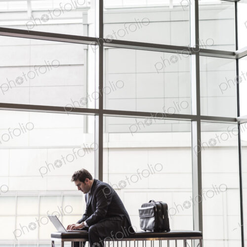 A businessman working on a laptop computer on a bench in a convention center lobby
