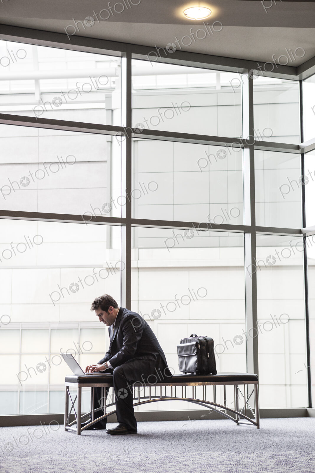 A businessman working on a laptop computer on a bench in a convention center lobby