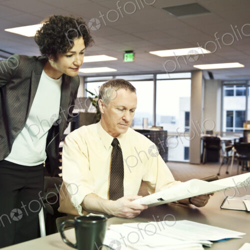 A businesswoman and a Caucasian businessman going over plans for a new space in their…