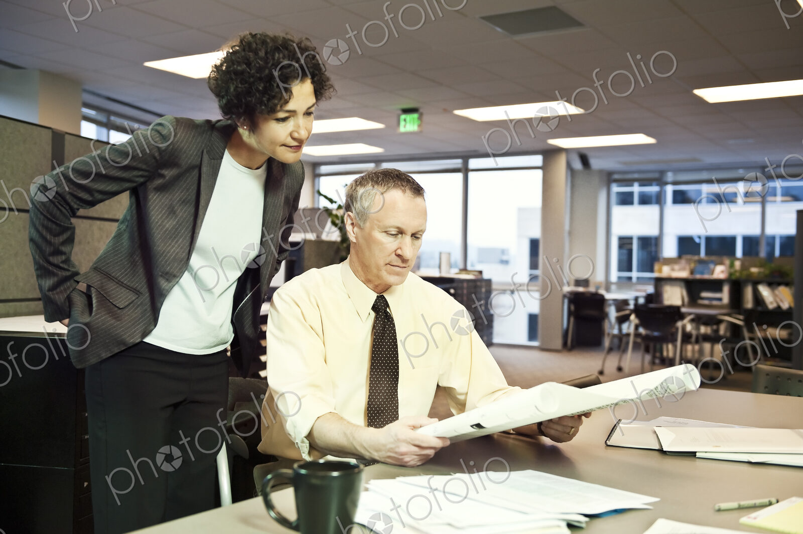 A businesswoman and a Caucasian businessman going over plans for a new space in their…