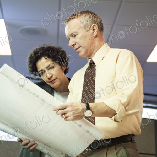 A businesswoman and a Caucasian businessman going over plans for an office A businesswoman and a Caucasian businessman going over plans for an office