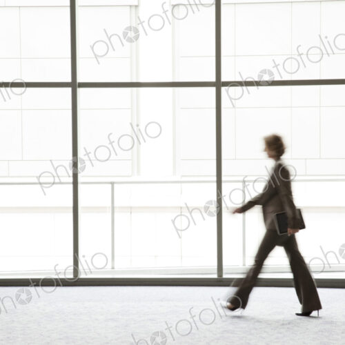 A businesswoman blurred in silhouette while walking past a large convention center window.