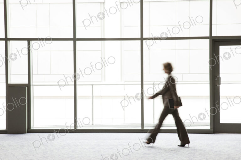 A businesswoman blurred in silhouette while walking past a large convention center window.