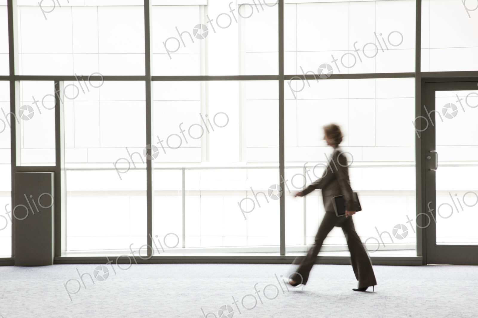 A businesswoman blurred in silhouette while walking past a large convention center window.