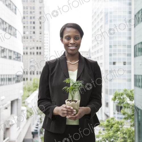 A businesswoman holding a small plant while stanidng next to a a large convention… A businesswoman holding a small plant while stanidng next to a a large convention…