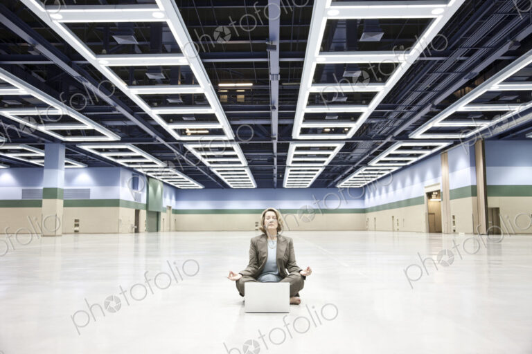 A businesswoman in a yoga pose with a laptop computer in the middle of a convention…