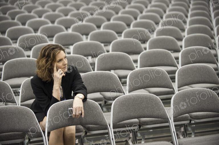 A businesswoman sitting alone in a room full of chairs prior to a meeting in a…