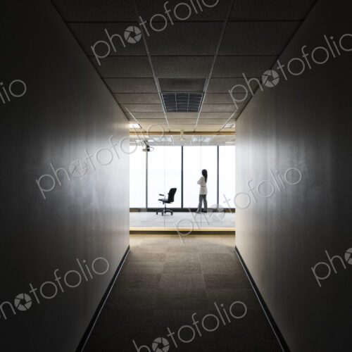 A businesswoman standing at a window at the end of a long hallway. A businesswoman standing at a window at the end of a long hallway.