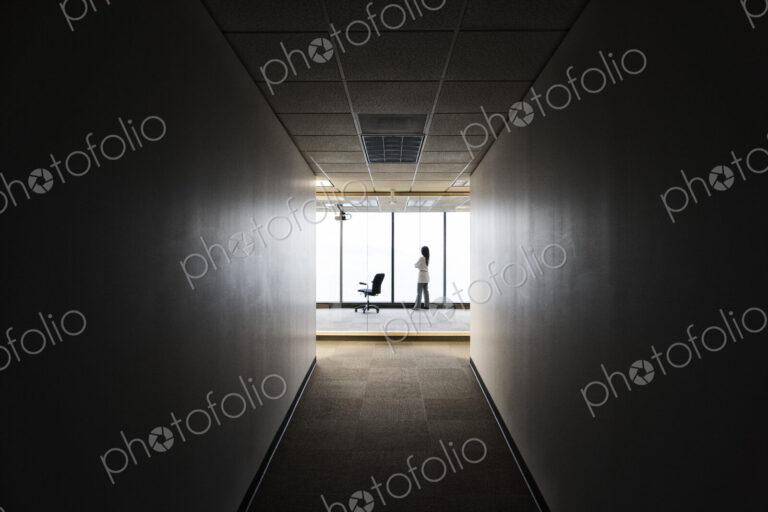 A businesswoman standing at a window at the end of a long hallway.