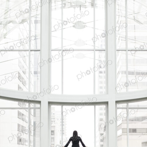 A businesswoman standing at a window in a large convention center lobby. A businesswoman standing at a window in a large convention center lobby.