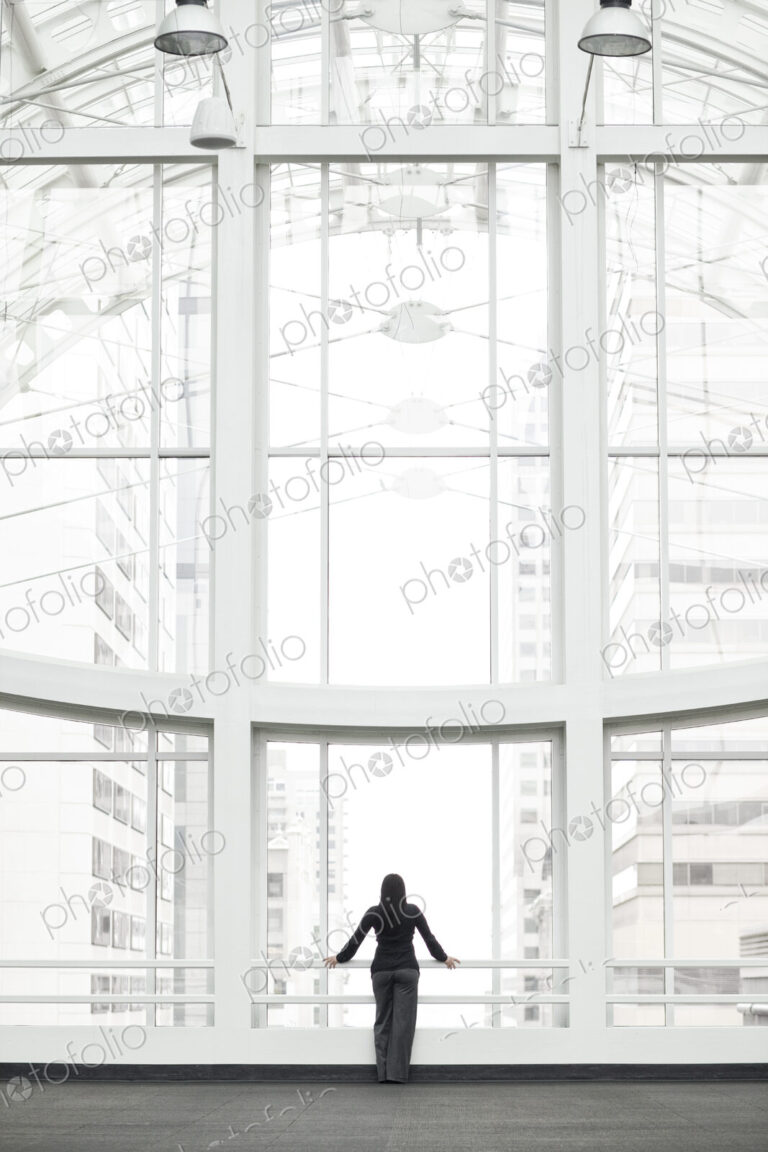 A businesswoman standing at a window in a large convention center lobby.
