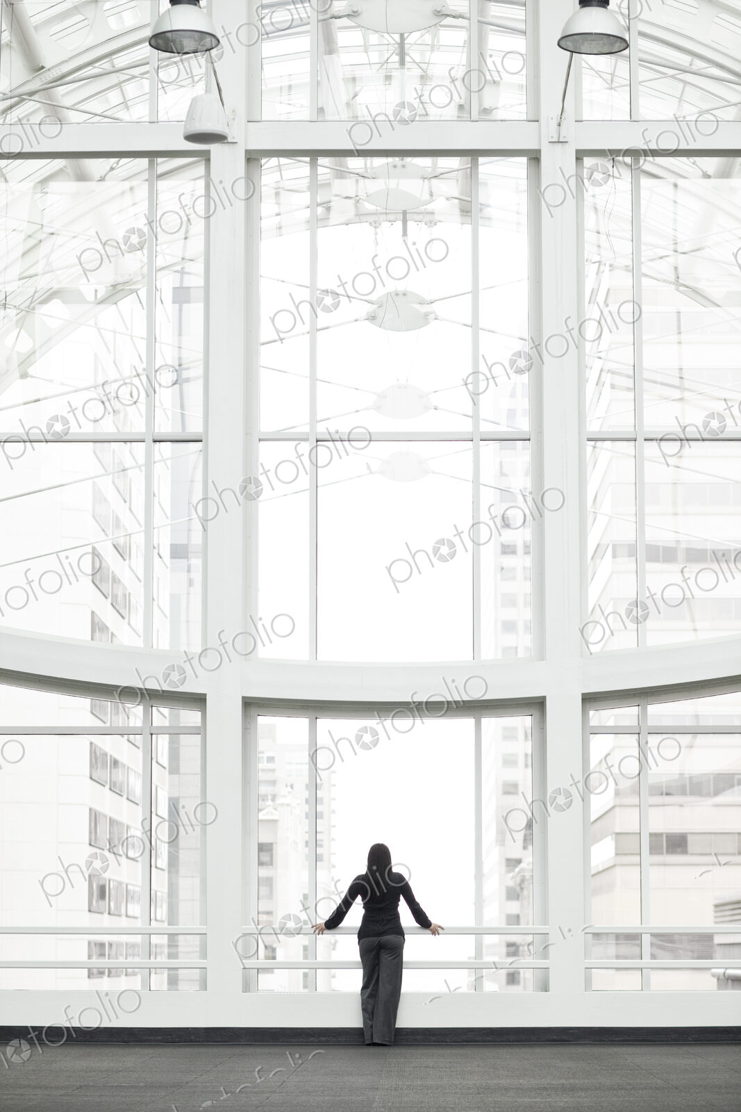 A businesswoman standing at a window in a large convention center lobby.