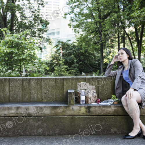 A businesswoman taking a break in a city park, seated on a bench with lunch. A businesswoman taking a break in a city park, seated on a bench with lunch.