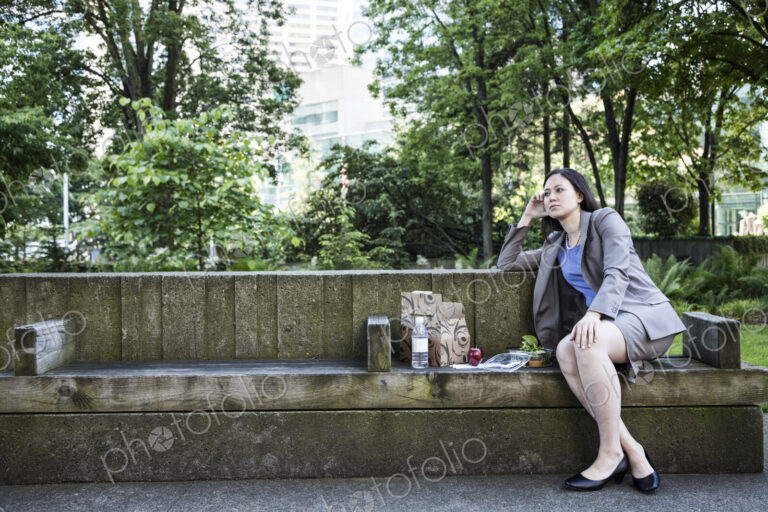 A businesswoman taking a break in a city park, seated on a bench with lunch.